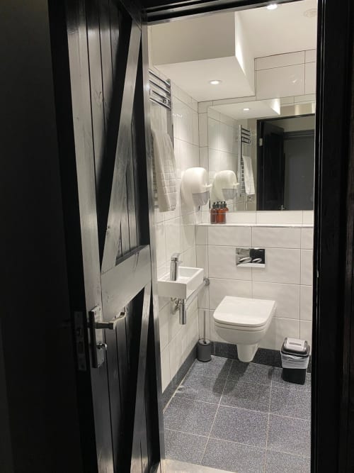 Modern bathroom at Stonegate Townhouse in York featuring white subway tiles, wall-mounted toilet, sink, large mirror, and