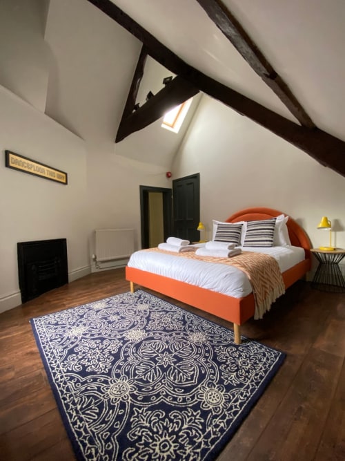 Bright loft bedroom in York's Stonegate Townhouse with orange bed, patterned rug, and exposed beams under skylight