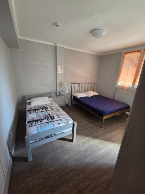 Chambre triple de l'hôtel Le Bel Air à Decize avec deux lits, parquet et vue sur la ville par fenêtre aux volets orange