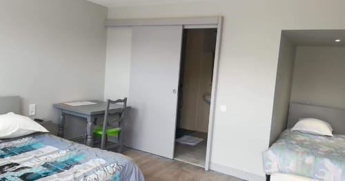 Chambre triple de l'hôtel Le Bel Air à Decize avec deux lits, bureau et porte coulissante vers la salle de bains