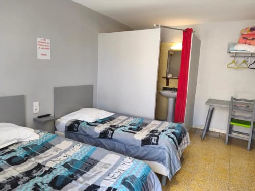 Chambre twin de l'hôtel Le Bel Air à Decize avec deux lits, têtes de lit grises et rideau rouge menant à la salle de bains