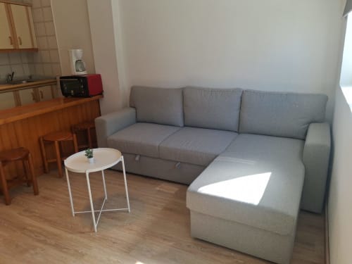 Gray sectional sofa with white side table in Sierra Nevada apartment living room with kitchenette and wooden floors