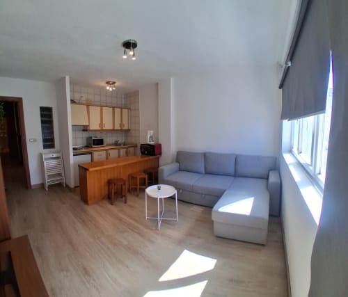 Bright apartment living room with gray sofa, wooden dining table, and kitchen at Sierra Nevada Center hotel in Granada