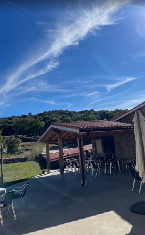 Terraza O Trancallo con pérgola de madera, zona de descanso y ladera boscosa bajo cielo azul despejado en Mourisca, Ourense