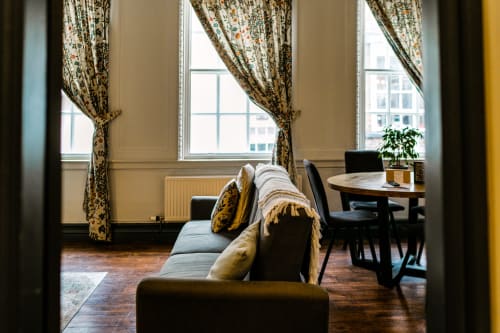 Elegant apartment living room with patterned curtains, gray sofa, wooden furniture, and city views at Stonegate Townhouse