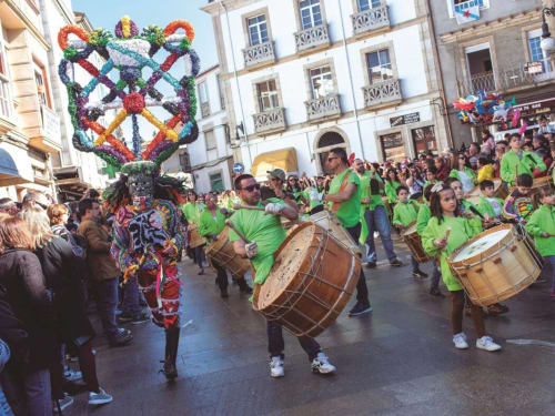 Vibrante desfile callejero en Ourense con tambores en camisetas verdes y decoraciones florales coloridas cerca de O Trancallo
