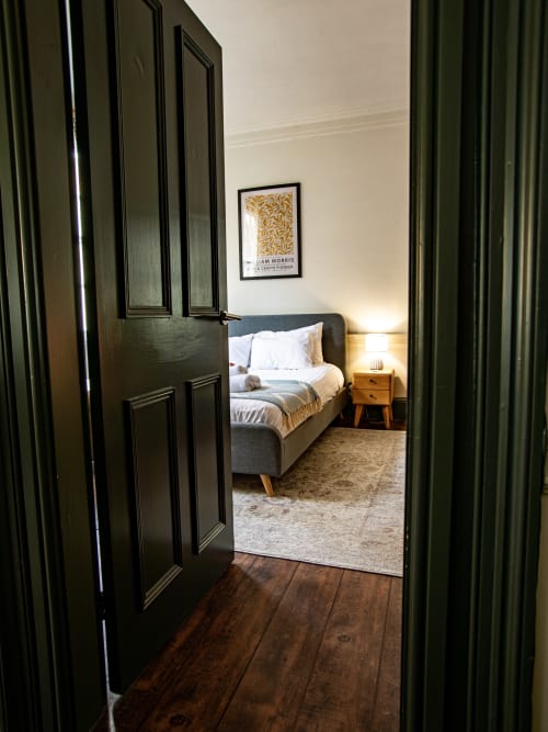 Black paneled doors opening into a bedroom at Stonegate Townhouse York, featuring a gray upholstered bed with white linens
