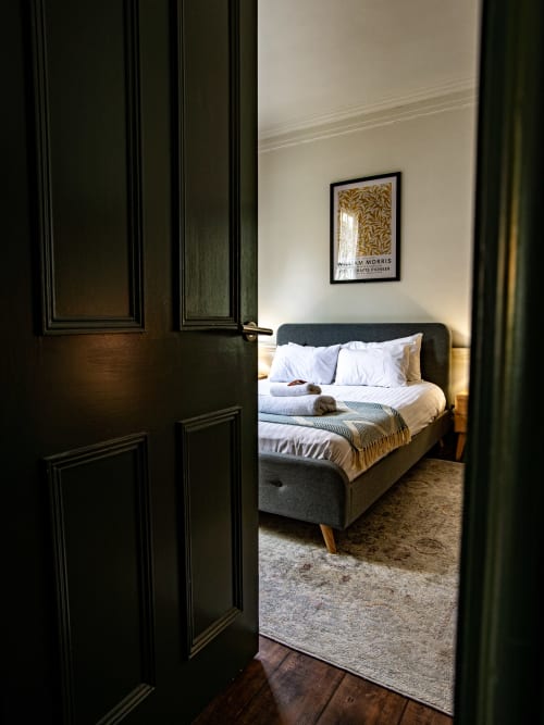 Black open doors reveal a bedroom at Stonegate Townhouse York, featuring a charcoal bed with white pillows and gold throw on