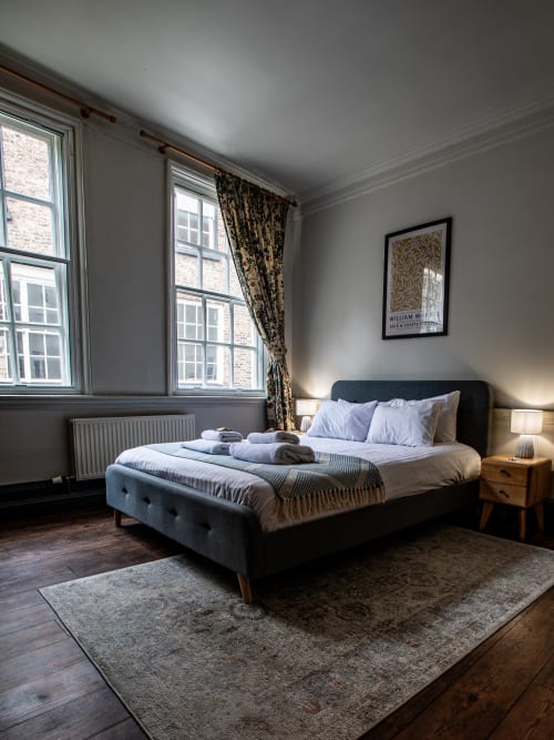 Spacious bedroom in Stonegate historic apartment, York with charcoal bed, wooden furniture, large windows and contemporary