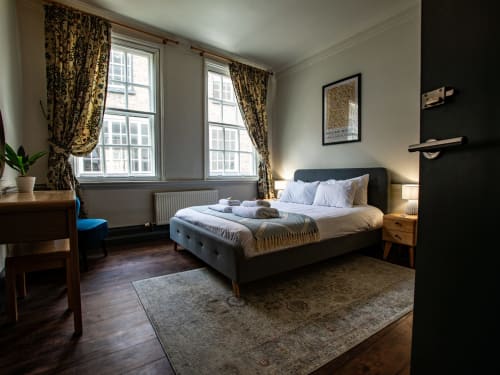 Elegant bedroom in Stonegate Townhouse York with dark headboard bed, large windows, patterned curtains, and wooden