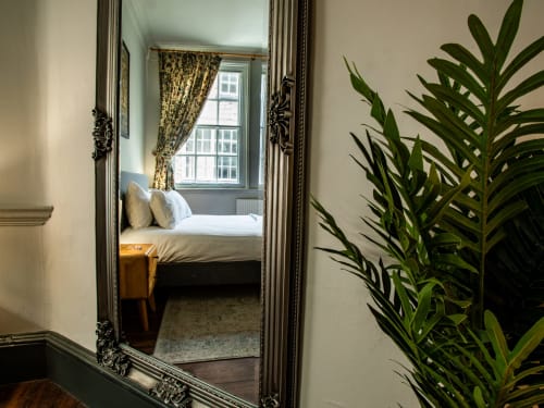 Ornate mirror reflecting bedroom in Stonegate Townhouse York apartment with bed, window, and potted plant visible