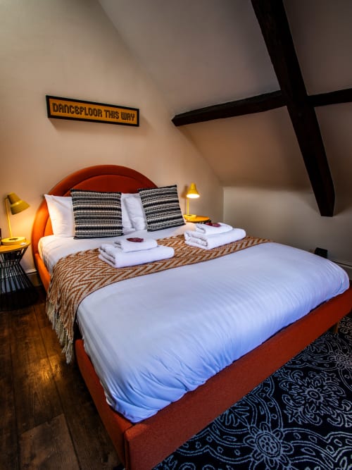 Modern bedroom at Stonegate Townhouse York with red bed frame, striped pillows, white linens, gold lamps, and 'Dancefloor