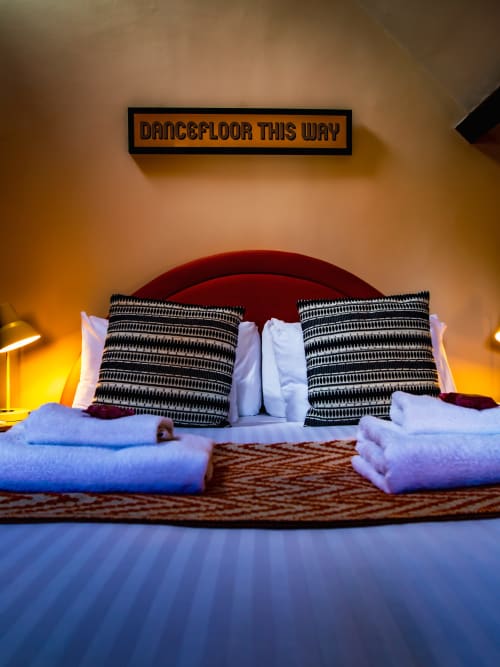 Modern bedroom with red headboard, patterned pillows, white towels, and orange wall at Stonegate Townhouse York