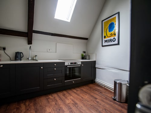 Modern kitchen in York apartment with black cabinets, stainless steel appliances, skylight, wooden floors, and Miró art print