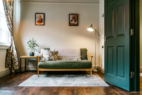 Bright apartment living room at Stonegate Townhouse York with green sofa, wooden frame, botanical wall art, and teal door