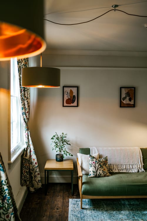 Cozy living room in York apartment with green sofa, patterned curtains, pendant lamp, potted plant, and botanical wall art.