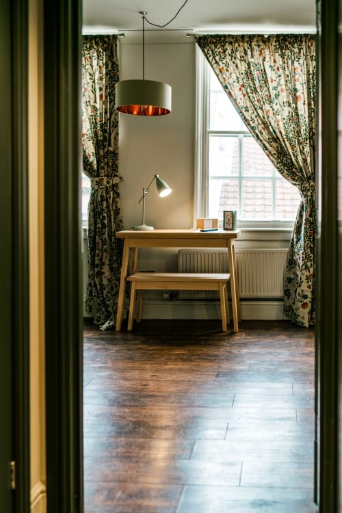 Dedicated workspace in York apartment with wooden desk, pendant lamp, floral curtains, and radiator by window