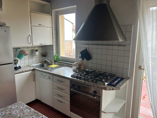 Cucina moderna in loft bolognese con fornello a gas, ante bianche, piano in granito e cappa nera