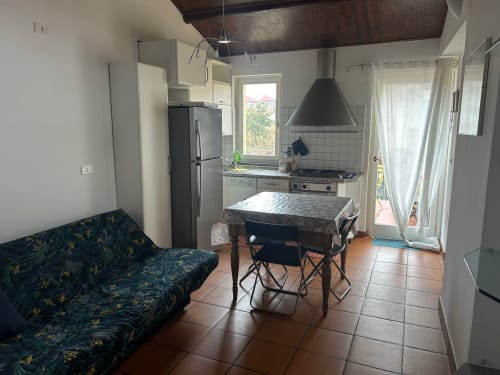 Cucina aperta e zona pranzo nell'appartamento di Bologna con stufa, tavolo, divano e porte vetrate verso il balcone
