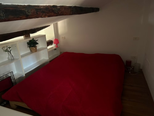 Camera da letto in soppalco con travi a vista e scaffali bianchi in appartamento bolognese