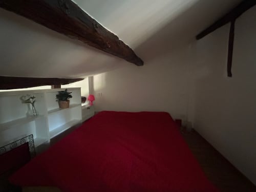Camera da letto in loft moderno a Bologna con biancheria rossa, travi a vista, scaffali bianchi con piante e vista sulla città a L'Appartamento