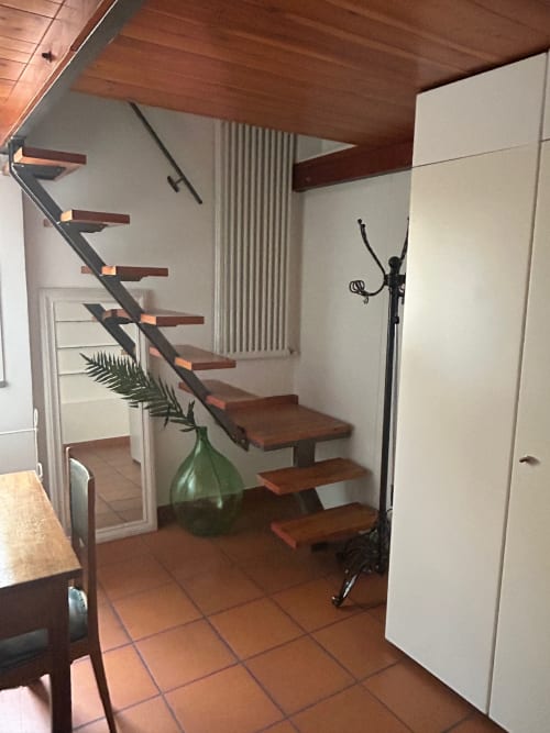 Scala moderna in loft a Bologna con gradini in legno, ringhiera metallica, pavimento in cotto e arredamento minimalista bianco