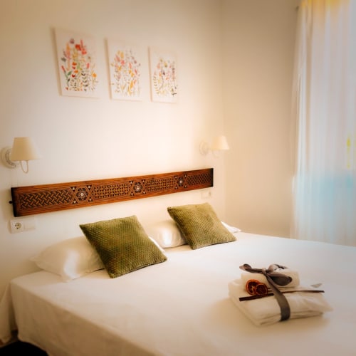 Cozy bedroom at Mas Ribas Hotel in Palamos with white bedding, green pillows, wooden headboard and floral artwork