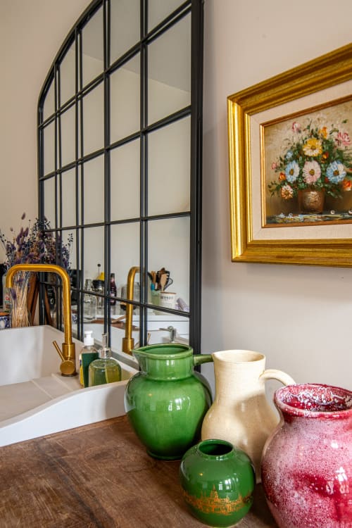 Vasque stylisée au B&B Bise de la Jouvence avec vases en céramique colorés, robinetterie dorée et miroir industriel noir