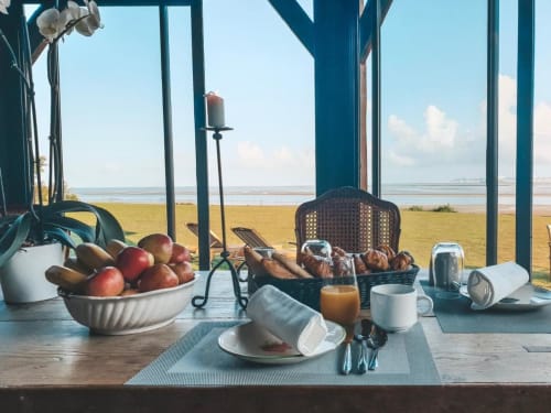 Table de petit-déjeuner à La Girelle avec vue sur la baie côtière, fruits frais, pâtisseries et boissons matinales à Honfleur
