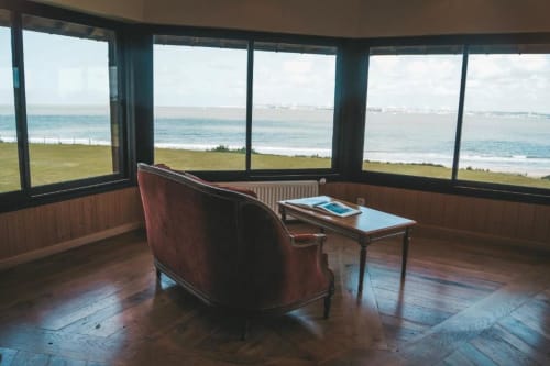 Suite panoramique à La Girelle à Honfleur avec vue mer, grandes fenêtres, fauteuil bordeaux et petite table