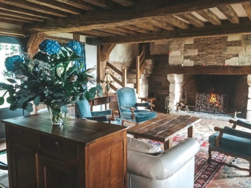 Salon rustique de la chambre d'hôtes La Girelle à Honfleur avec poutres apparentes, cheminée, fauteuils bleus et fleurs