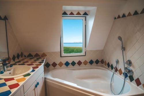 Salle de bain aux carreaux géométriques colorés, baignoire, lavabo et fenêtre de toit offrant une vue sur la mer à La Girelle, Honfleur