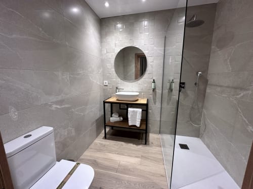 Baño moderno del Hotel Síbel Baza con azulejos de mármol, lavamanos tipo vasija, ducha a ras de suelo y tocador de madera