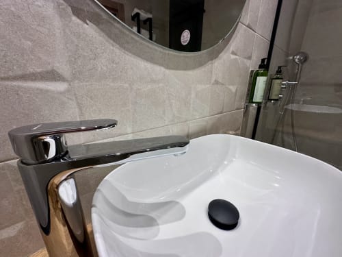 Moderno lavabo blanco con grifo negro en el Hotel Síbel Baza, espejo redondo