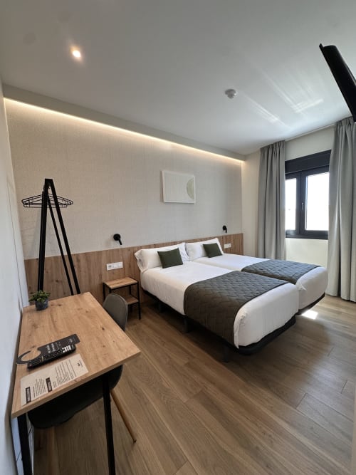 Moderna habitación doble en Hotel Síbel Baza con camas gemelas, escritorio de madera, pared beige y vistas a la montaña desde la ventana