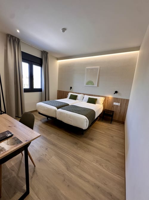 Moderno dormitorio doble en Hotel Síbel Baza con camas gemelas, escritorio de madera y vistas a las montañas desde la ventana