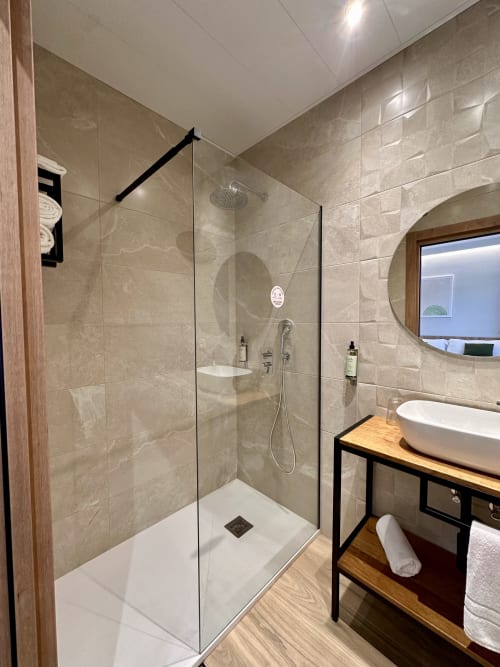 Baño moderno con mampara de ducha de vidrio en Hotel Síbel Baza, paredes de azulejos beige y mueble de madera