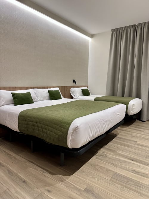 Moderno dormitorio triple del Hotel Síbel Baza con camas individuales, ropa de cama verde y vistas a la montaña en Baza, España
