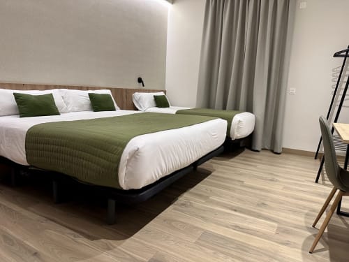 Moderna habitación triple del Hotel Síbel Baza con ropa de cama verde, suelo de madera y cortinas con vista a las montañas