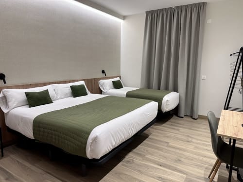 Moderna habitación triple del Hotel Síbel Baza con dos camas, detalles verdes y vistas a las montañas de Baza