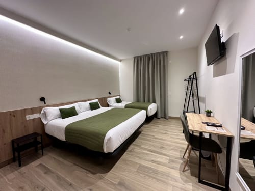 Habitación triple moderna en Hotel Síbel Baza con camas gemelas, detalles en verde, escritorio, TV pantalla plana y vistas a la montaña