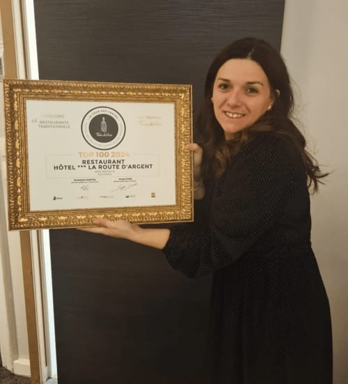 Femme tenant le prix TOP 100 2024 du restaurant Hôtel La Route d'Argent à Bozouls
