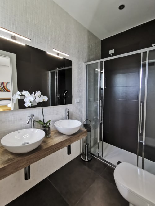 Modern bathroom at Green Land Boutique Hotel with dual vessel sinks, black tile accent wall, walk-in shower, and white