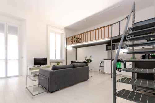 Moderno appartamento a Milano con letto in soppalco, divano grigio, TV e scala in metallo in luminoso open space