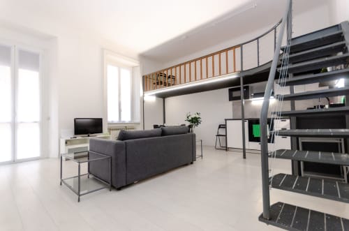 Moderno loft a Milano con soppalco, divano grigio, TV e scala in metallo