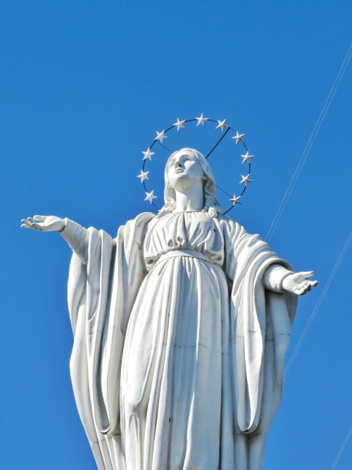 Statua bianca con alone e braccia aperte contro il cielo blu a Campagnano di Roma