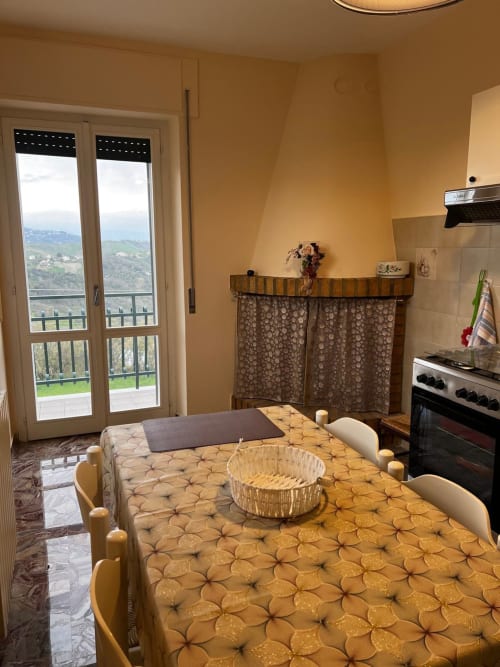 Cucina-soggiorno soleggiata nell'appartamento di Atessa con tavolo, fornello e balcone vista campagna