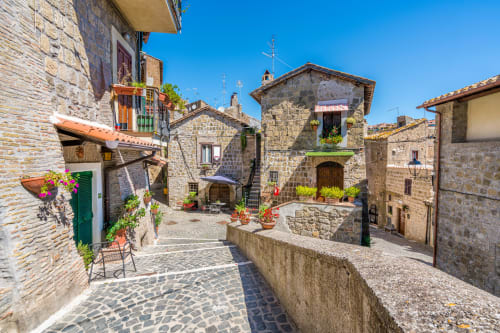 Piazza medievale in pietra a Campagnano di Roma con architettura storica, fiori in vaso e cielo azzurro