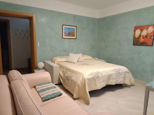 Accogliente camera d'hotel Tales of Abruzzo ad Atessa con pareti verde menta, biancheria color crema e zona relax rosa