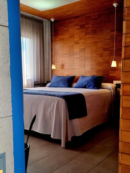 Modern bedroom at El Arrecife de Conil hotel with wooden walls, double bed, blue pillows, and pendant lighting in Conil de la
